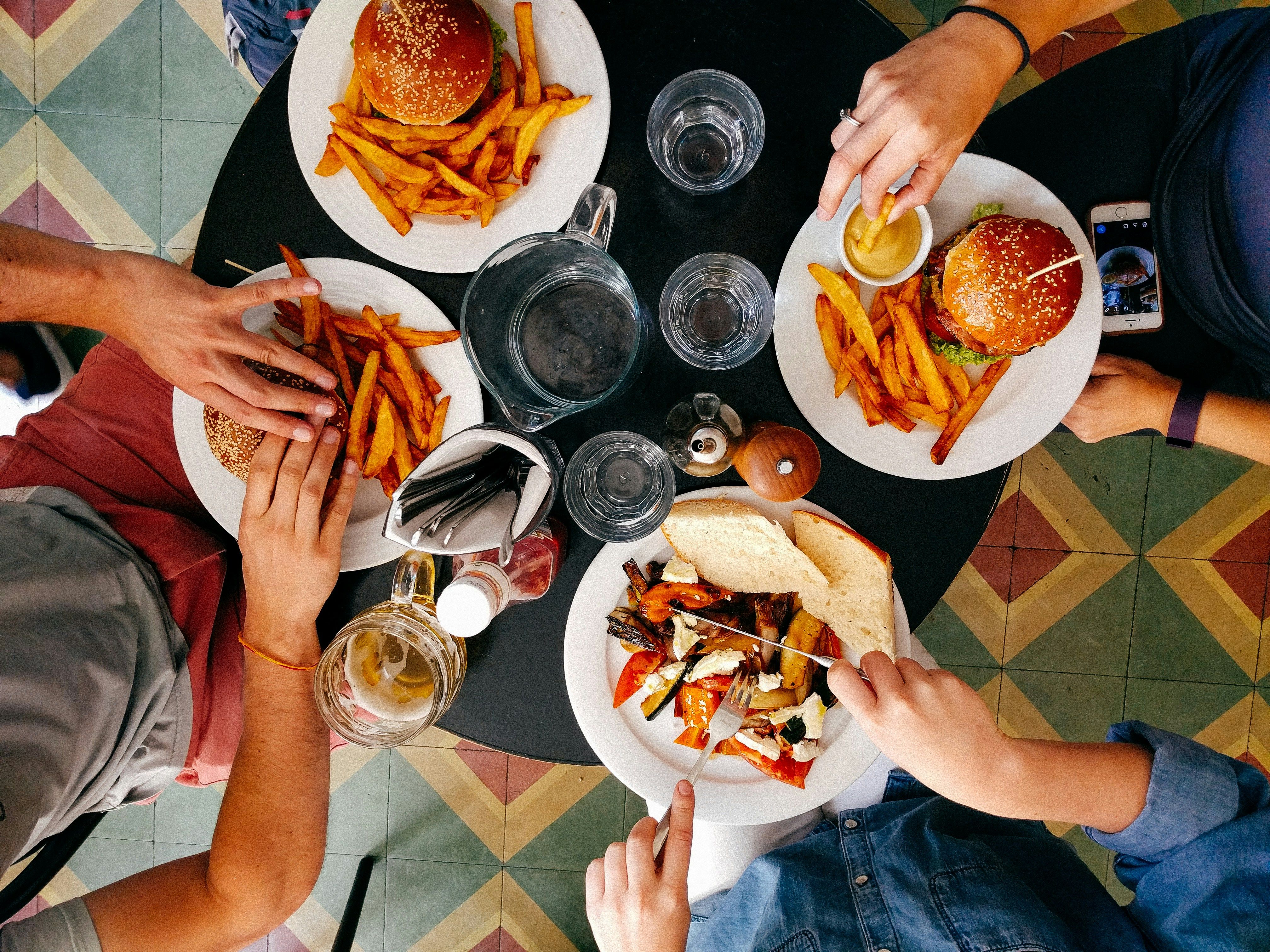Top-down view of three people eating burgers, fries, and sandwiches at a restaurant table