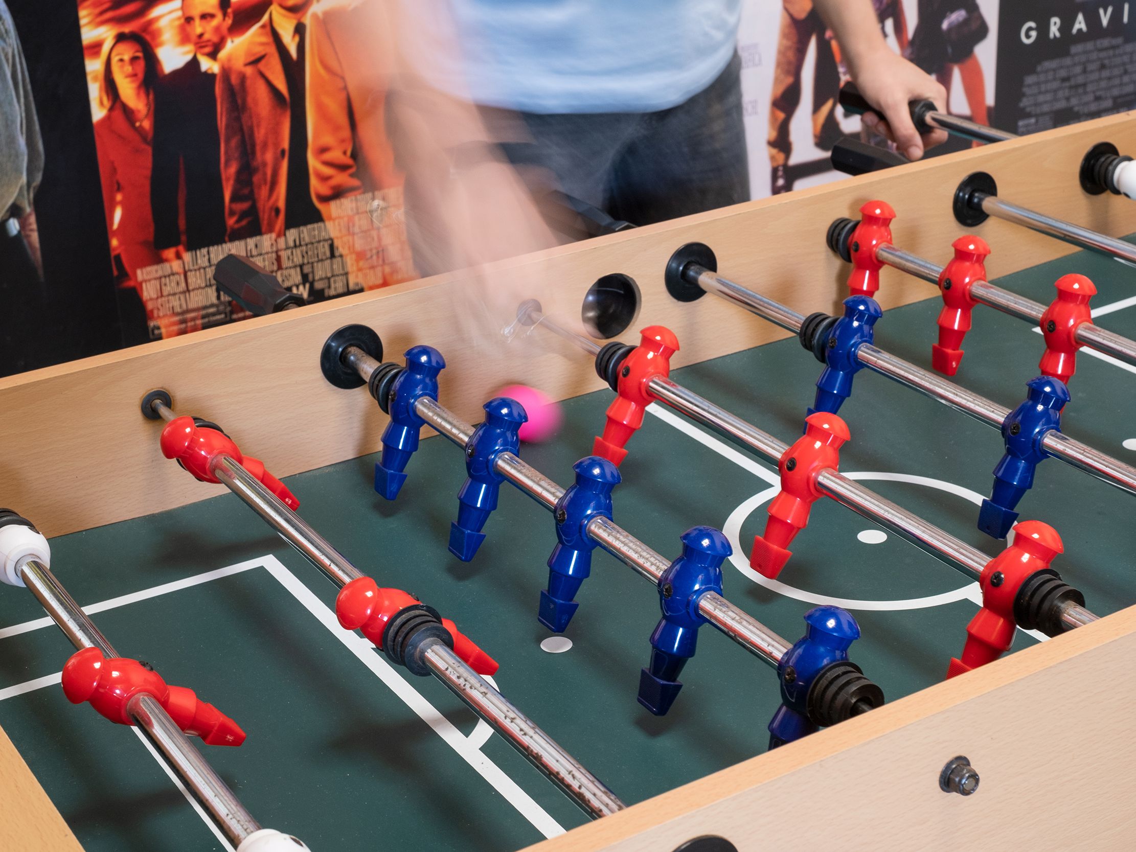 People playing foosball with red and blue players on a green table
