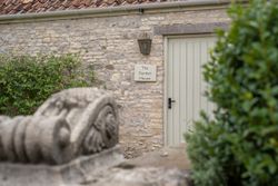A garden house door with a sign reading 'The Garden House' on a stone wall, surrounded by greenery.