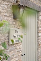 Sign reading 'The Garden House' mounted on a stone wall next to a wooden door and lantern