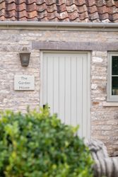 Front door of a stone house labeled 'The Garden House' with a lamp above and some greenery in the foreground.
