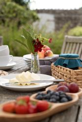 Outdoor table setting with fruit, butter, jam, and a vase of flowers