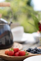 A close-up of fresh strawberries and blueberries in a wooden dish on an outdoor table.