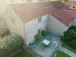 Aerial view of a stone house with a red tiled roof and patio area