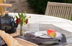 Outdoor table setting with teapot, baguette, flowers, cups, plates, apples, and cutlery
