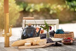 Outdoor breakfast table set with bread, a teapot, fruit, and jam.