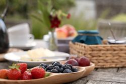 A wooden tray with strawberries, blueberries, and plums on a rustic outdoor table set for breakfast.