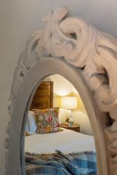 Reflection of a cozy bedroom with a floral pillow and bedside lamp in an ornate mirror