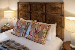 A cozy bed with a wooden carved headboard, floral pillows, and bedside tables with lamps.