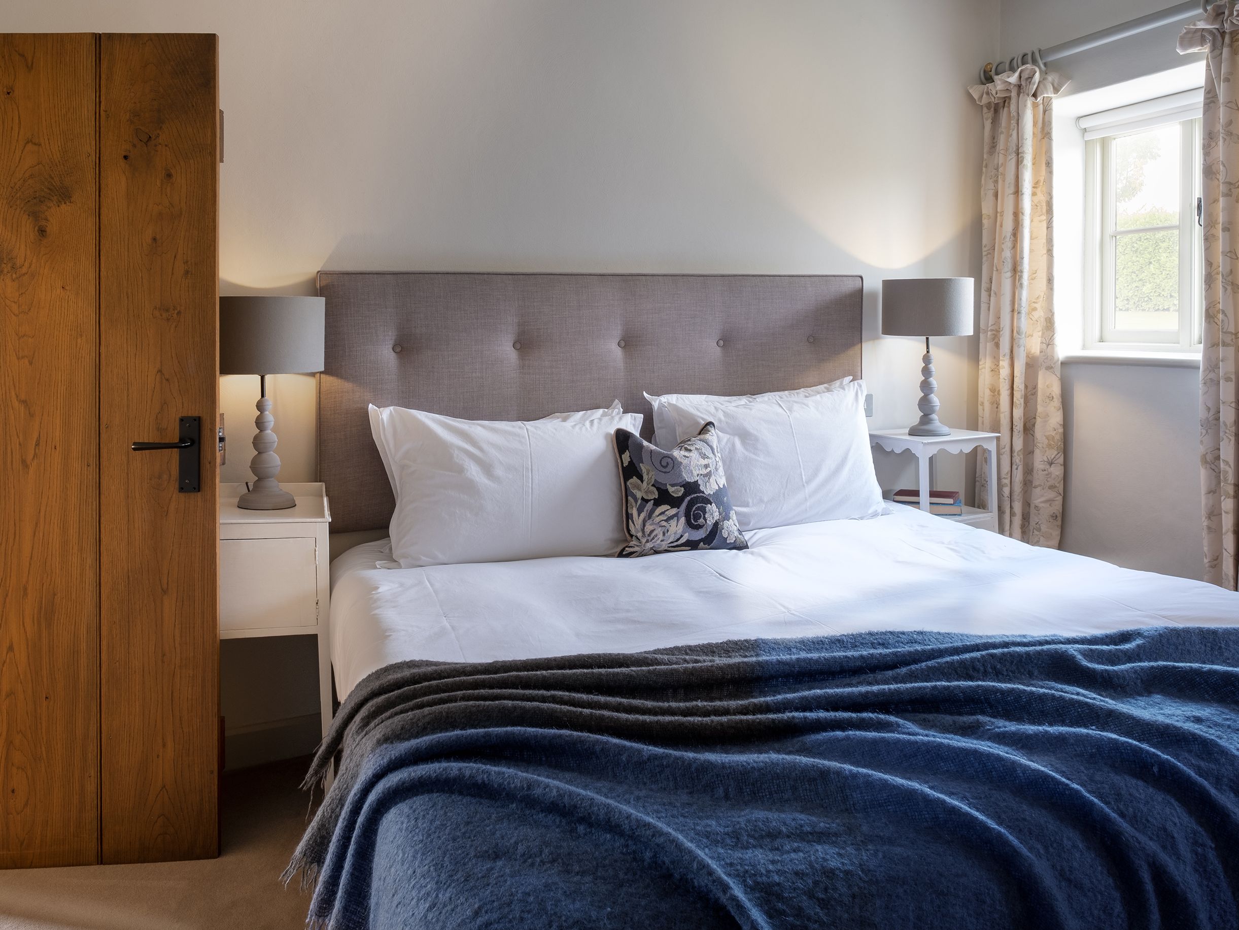 Cozy bedroom with a large bed, gray headboard, white bedding, blue blanket, and two bedside tables with lamps.