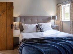 Cozy bedroom with a large bed, gray headboard, white bedding, blue blanket, and two bedside tables with lamps.