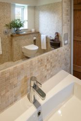 Modern bathroom with wall-mounted toilet, sink, and a vase with green leaves on the windowsill.