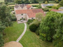 Aerial view of a traditional stone house with red tiled roof, surrounded by a well-kept garden and trees.