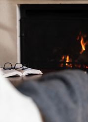 A pair of eyeglasses resting on an open book with a fireplace burning in the background.