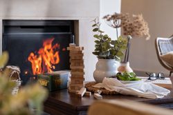 Cozy living room scene with a game of Tumbling Tower, a vase of greenery, a bowl of fruit, and a fireplace in the background.