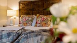 Cozy bedroom with floral pillows, wooden headboard, and bedside lamp