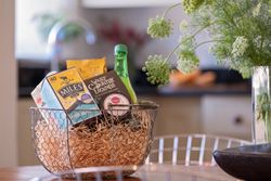 Wire basket with assorted snacks and drinks on a table next to a vase of green flowers.