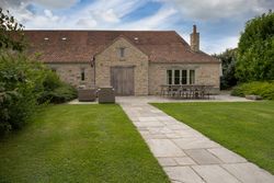 Traditional stone house with a red-tiled roof, outdoor seating area, and a stone pathway across a green lawn.