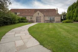 Stone house with red tiled roof and a paved walkway leading through a green lawn