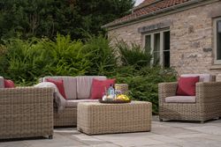 Outdoor patio seating area with wicker furniture, red cushions, and a stone house in the background.