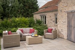 Patio area with wicker furniture, red cushions, a coffee table with drinks, and a stone house backdrop.