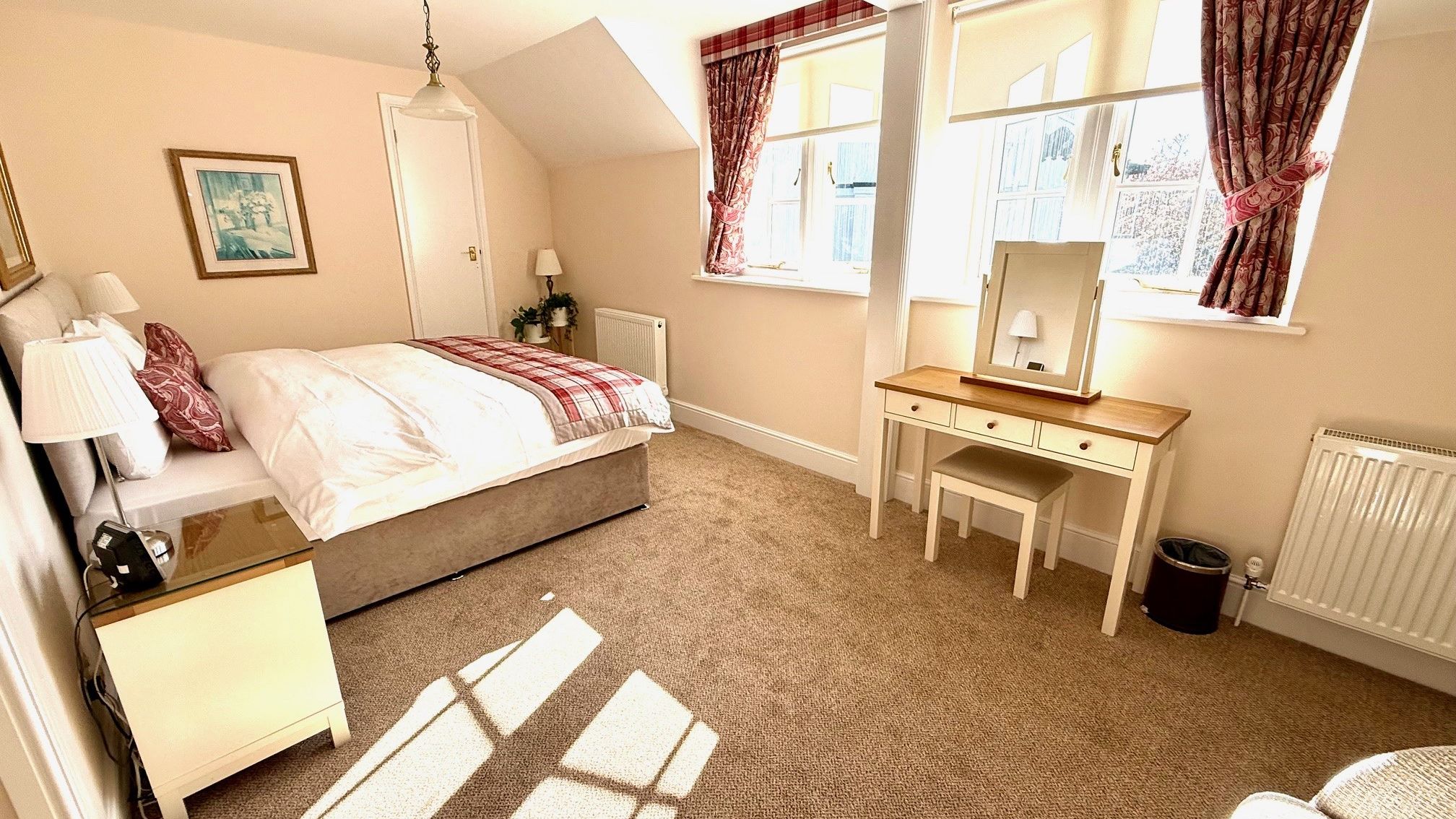 Bright first-floor bedroom with double bed, bedside table and dressing table by large windows with patterned curtains