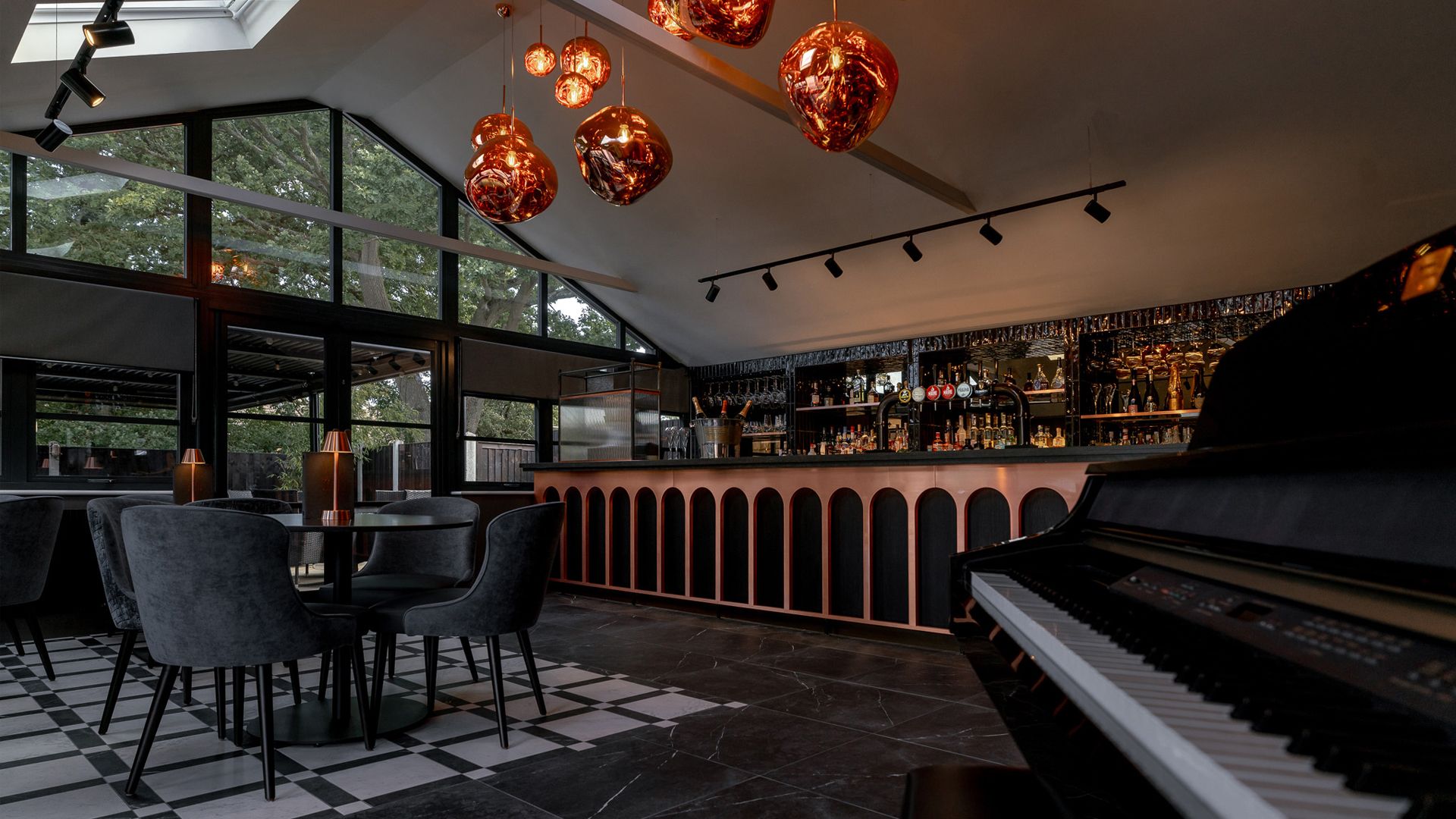 Modern bar interior with large windows, velvet chairs, a stylish bar counter, and a piano in the foreground