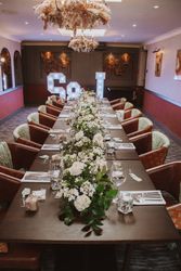 Elegant dining table set for an event, decorated with white flowers and greenery, with illuminated letters in the background.