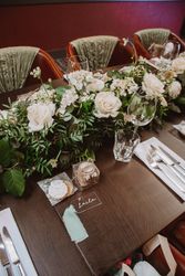 Elegant wedding table setting with white roses, greenery, and personalized gifts.