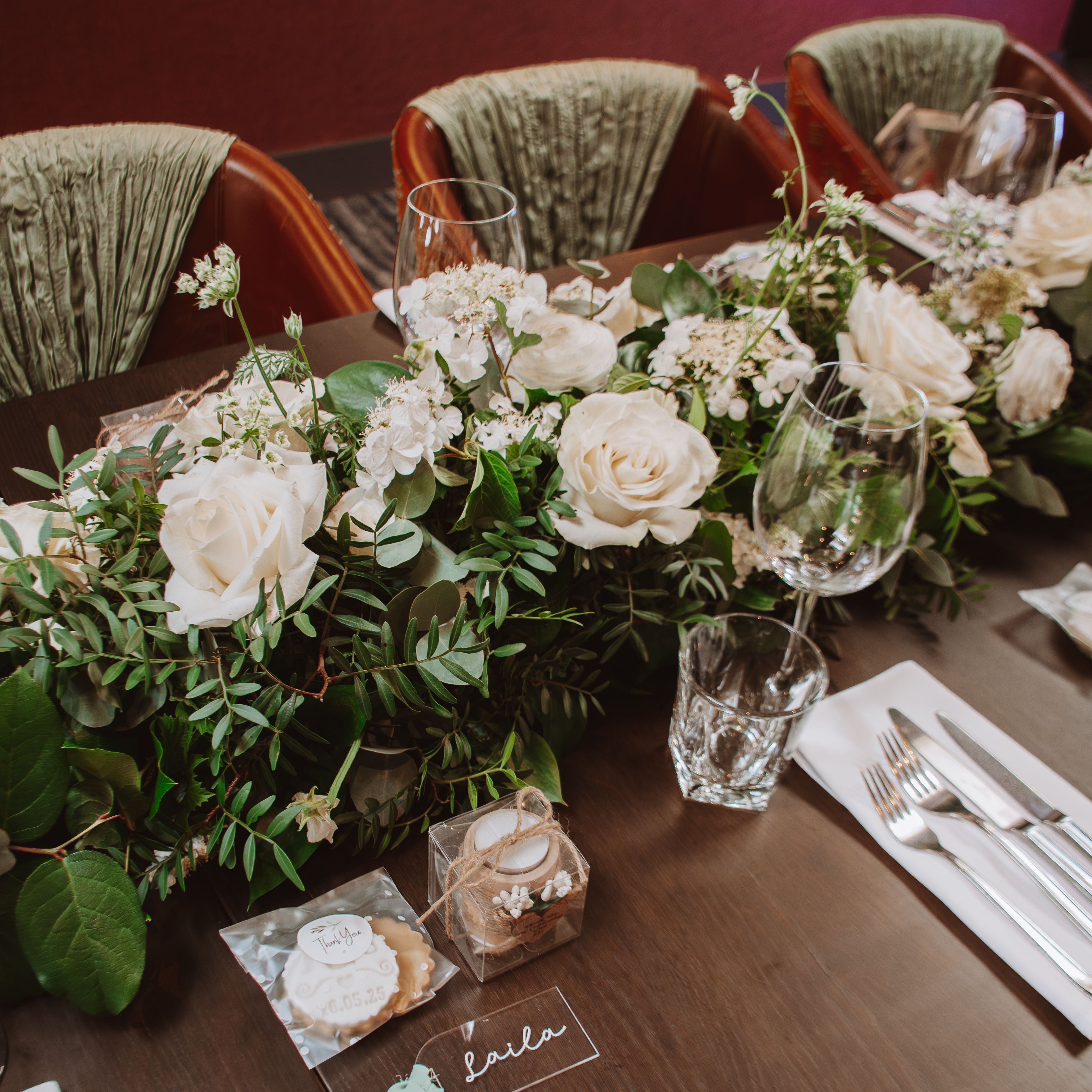 Elegant wedding table setting with white roses, greenery, and personalized gifts.