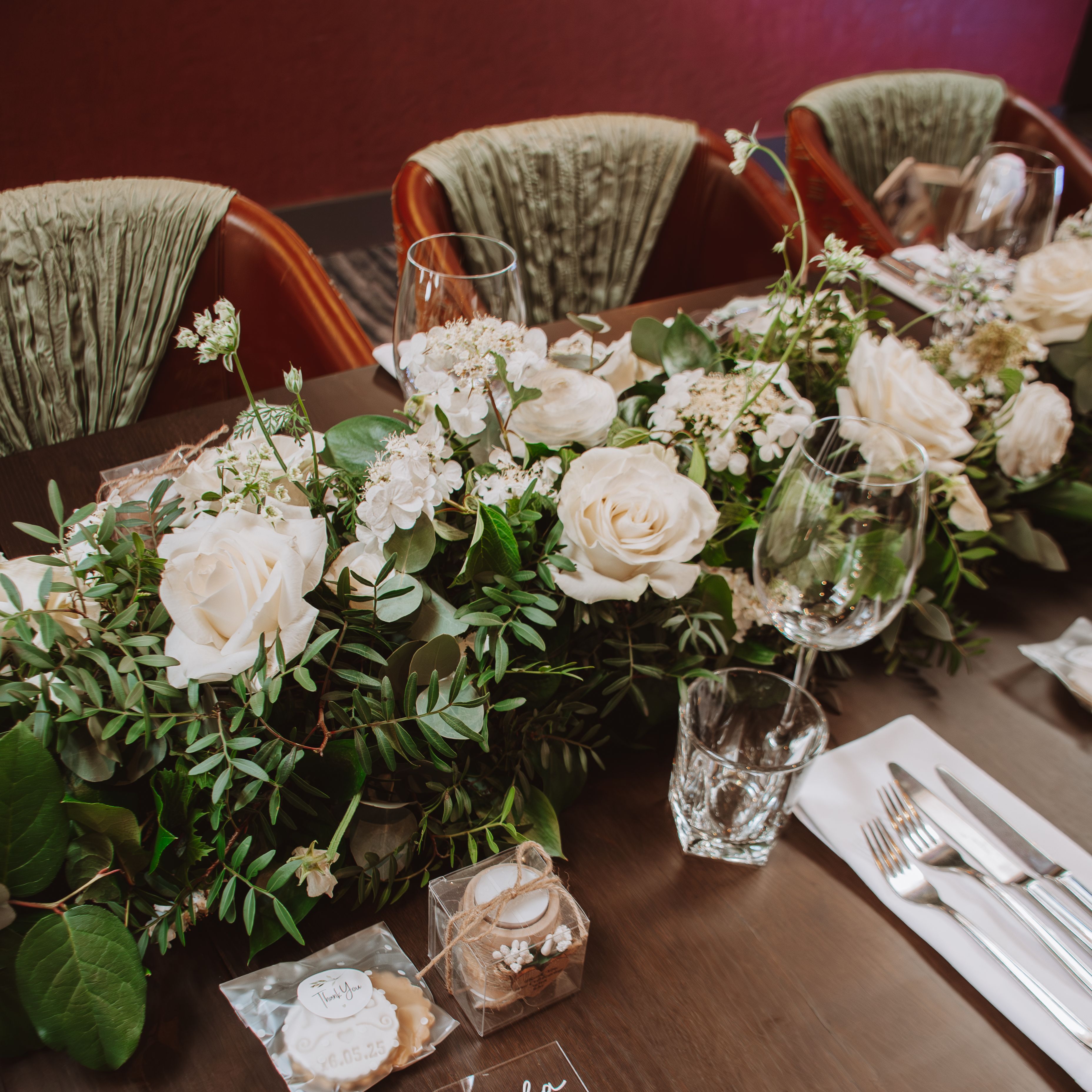 Elegant wedding table setting with white roses, greenery, and personalized gifts.