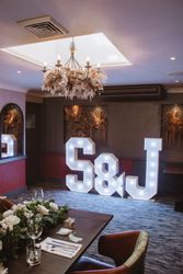 Illuminated large letters S & J in a decorated room with floral arrangements and a chandelier above.