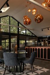 Modern bar area with velvet chairs, geometric pendant lights, large windows, and a sleek counter.