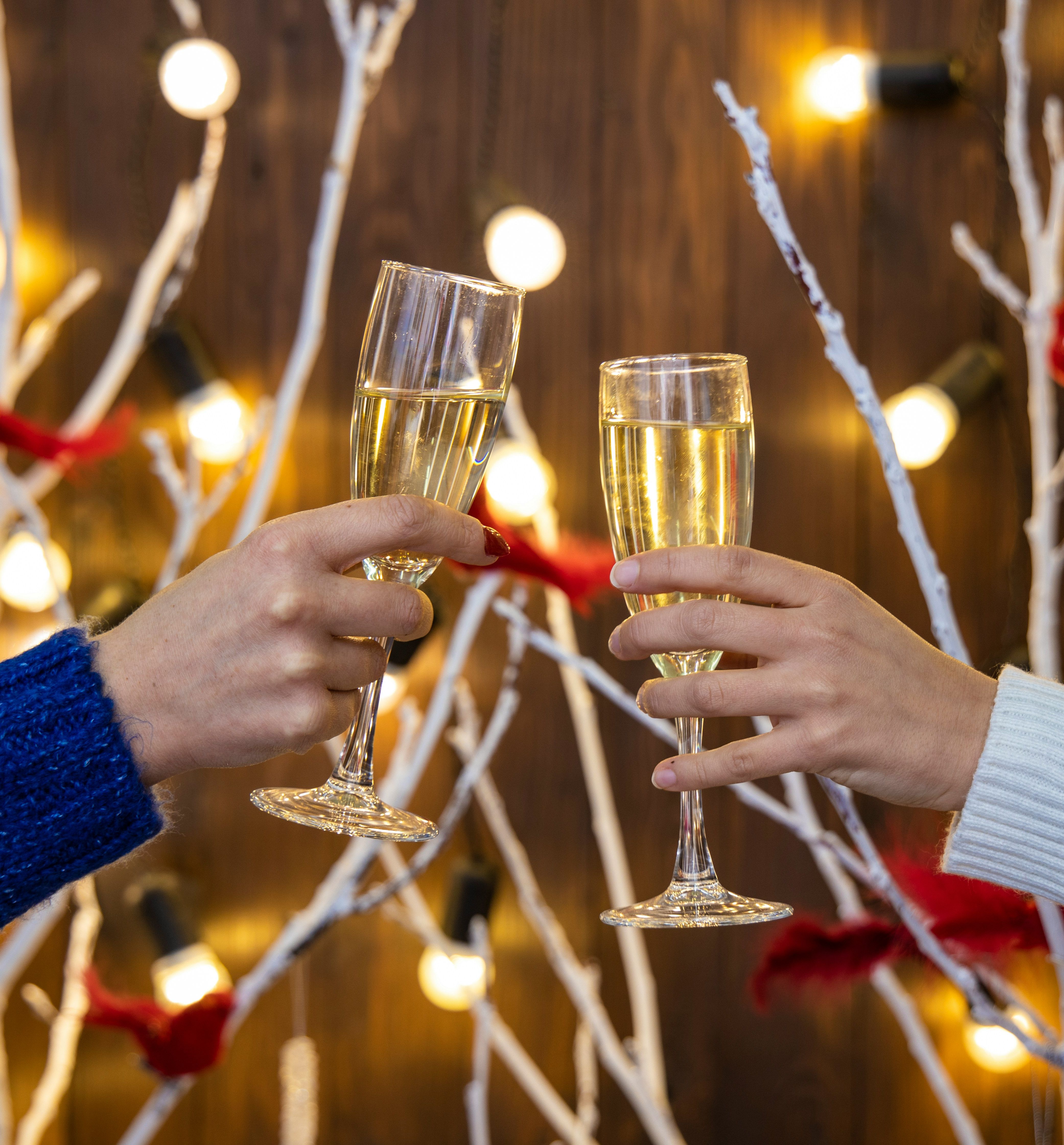 Two people clinking champagne glasses in front of festive lights and decorated white branches