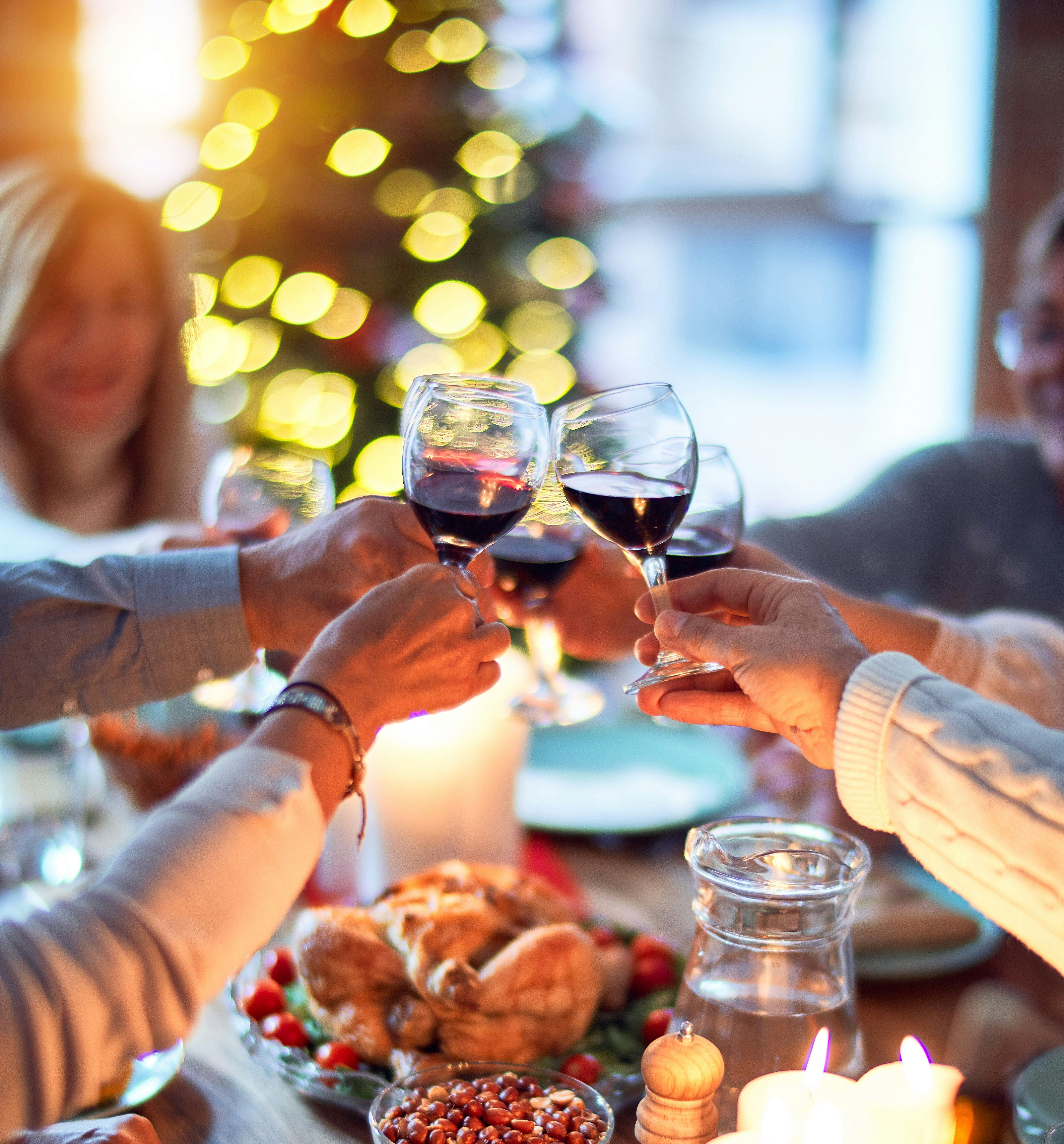 People clinking glasses of red wine at a festive dinner table with food and candles.