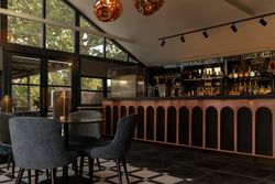 Modern bar area with arched counter, velvet chairs, and large windows overlooking trees.
