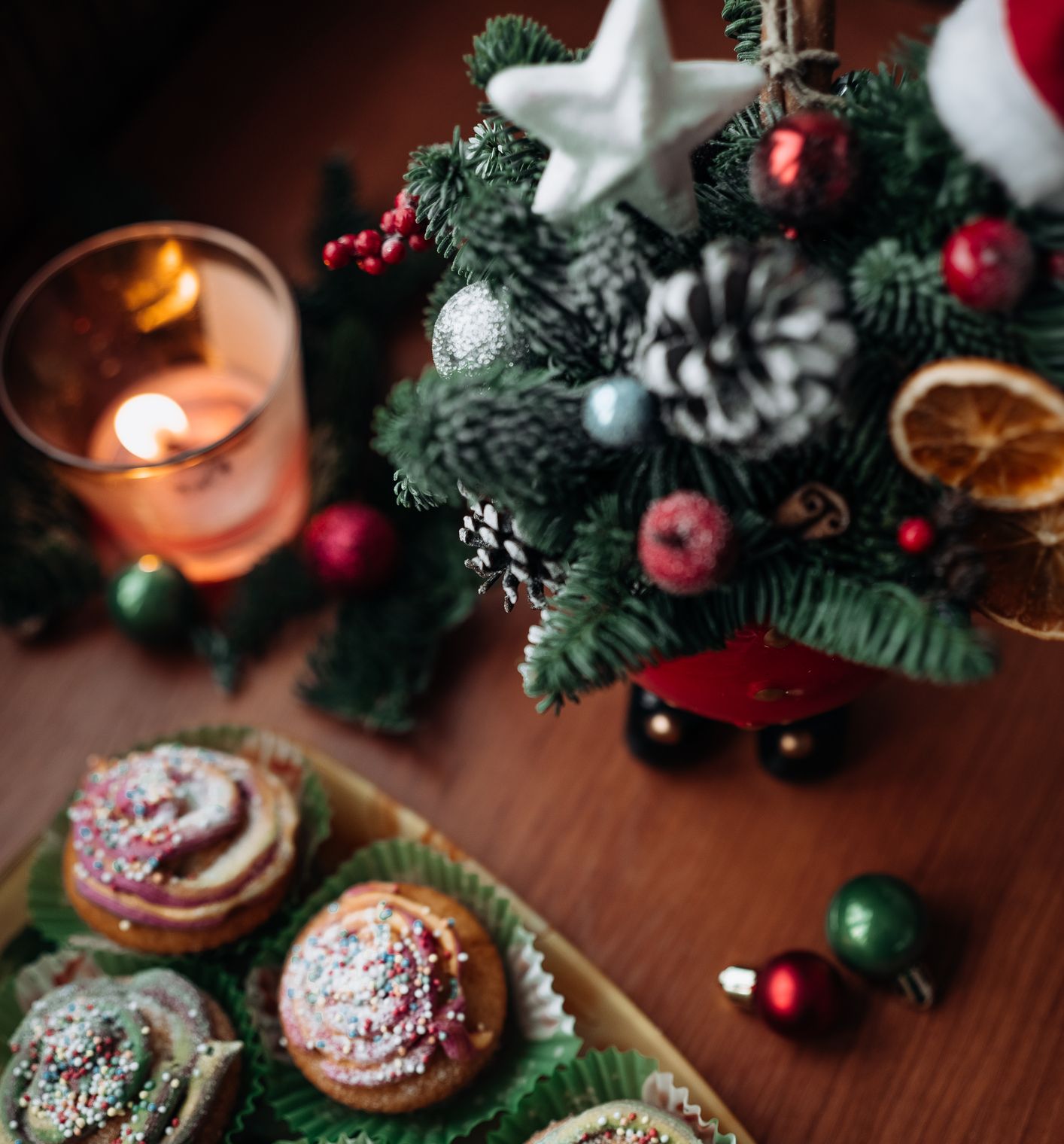 Christmas cupcakes with colorful sprinkles next to a small decorated Christmas tree and a lit candle