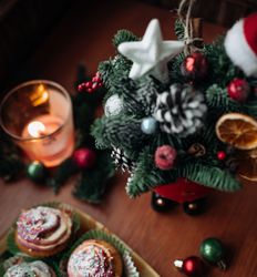 Christmas cupcakes with colorful sprinkles next to a small decorated Christmas tree and a lit candle