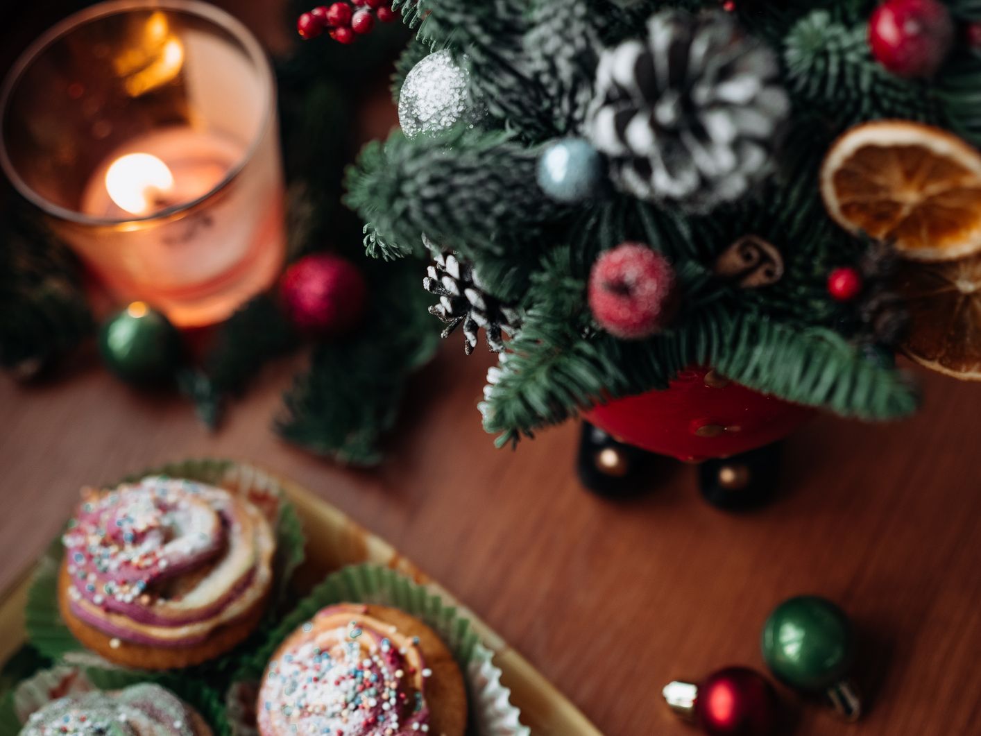 Christmas cupcakes with colorful sprinkles next to a small decorated Christmas tree and a lit candle