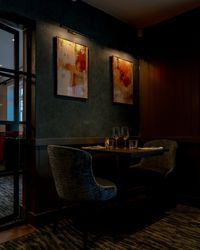 A dimly lit restaurant table set for two, with two glasses, two chairs, and abstract art hanging on the wall above.