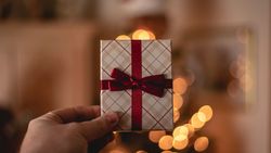 Hand holding a wrapped gift with a red ribbon in front of blurred holiday lights