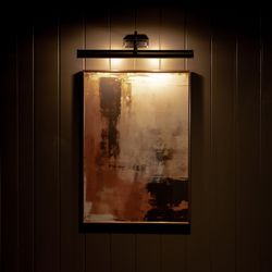 Abstract painting illuminated by a picture light on a dark paneled wall