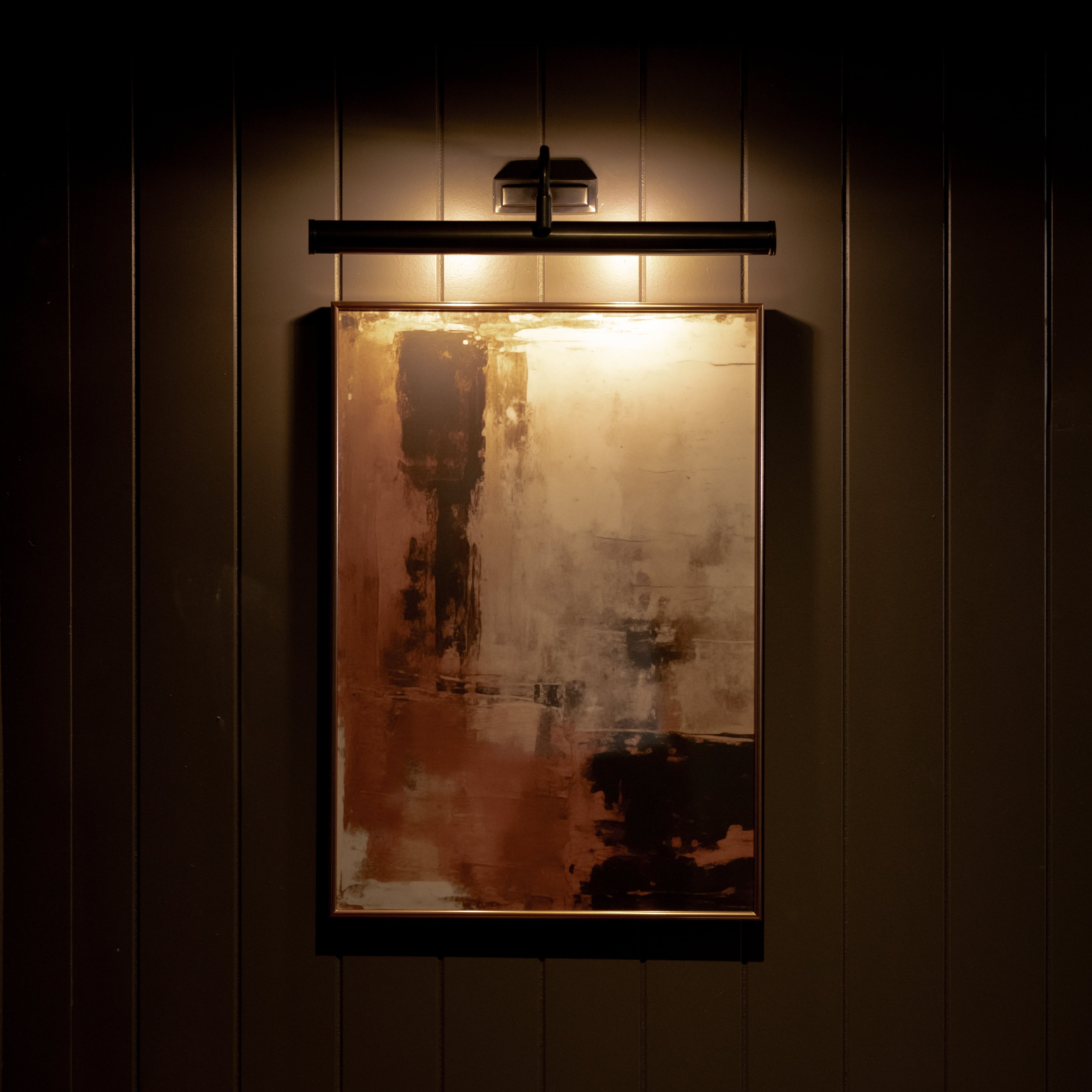 Abstract painting illuminated by a picture light on a dark paneled wall
