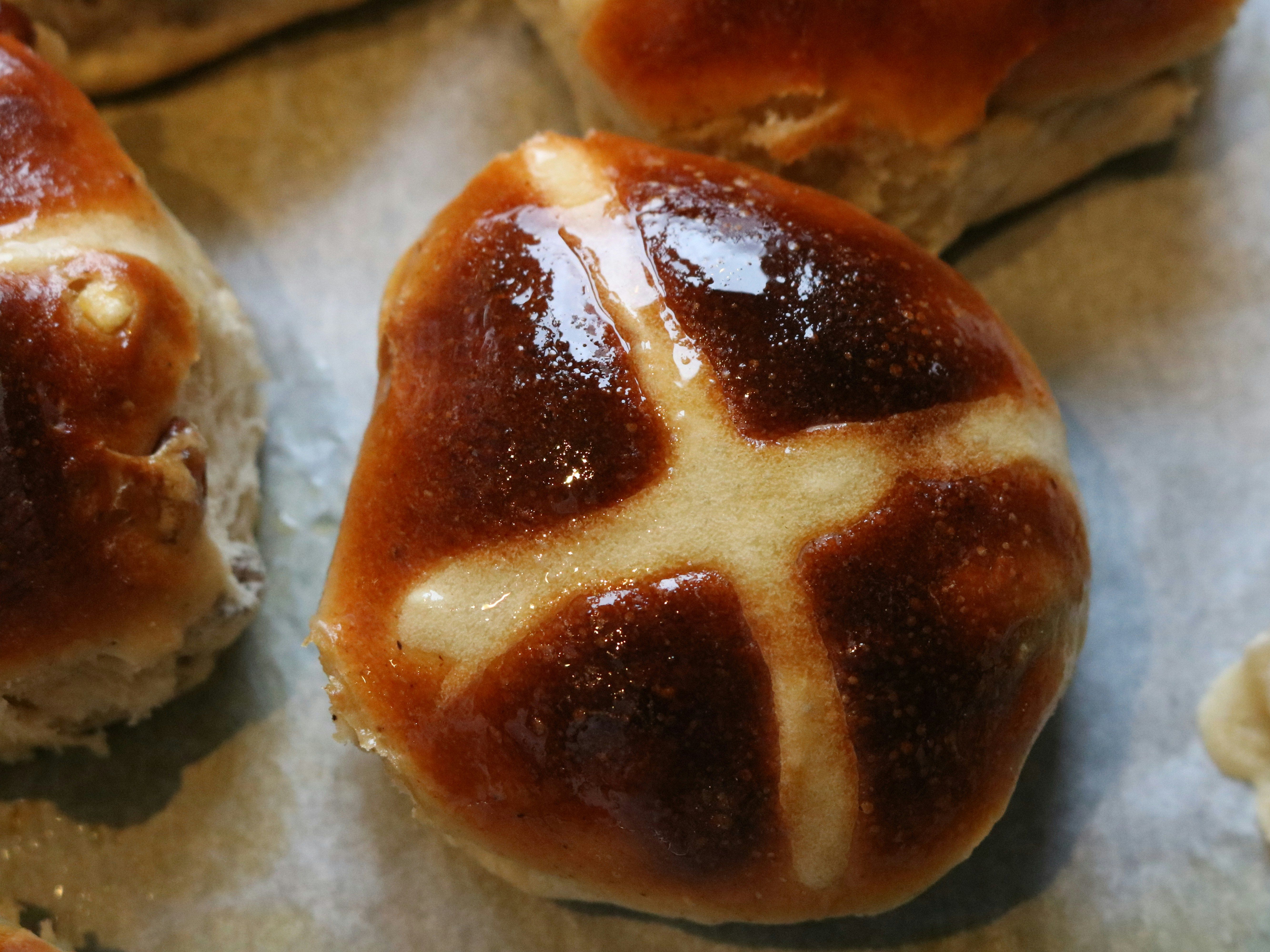 Close-up of a glazed hot cross bun on a baking tray