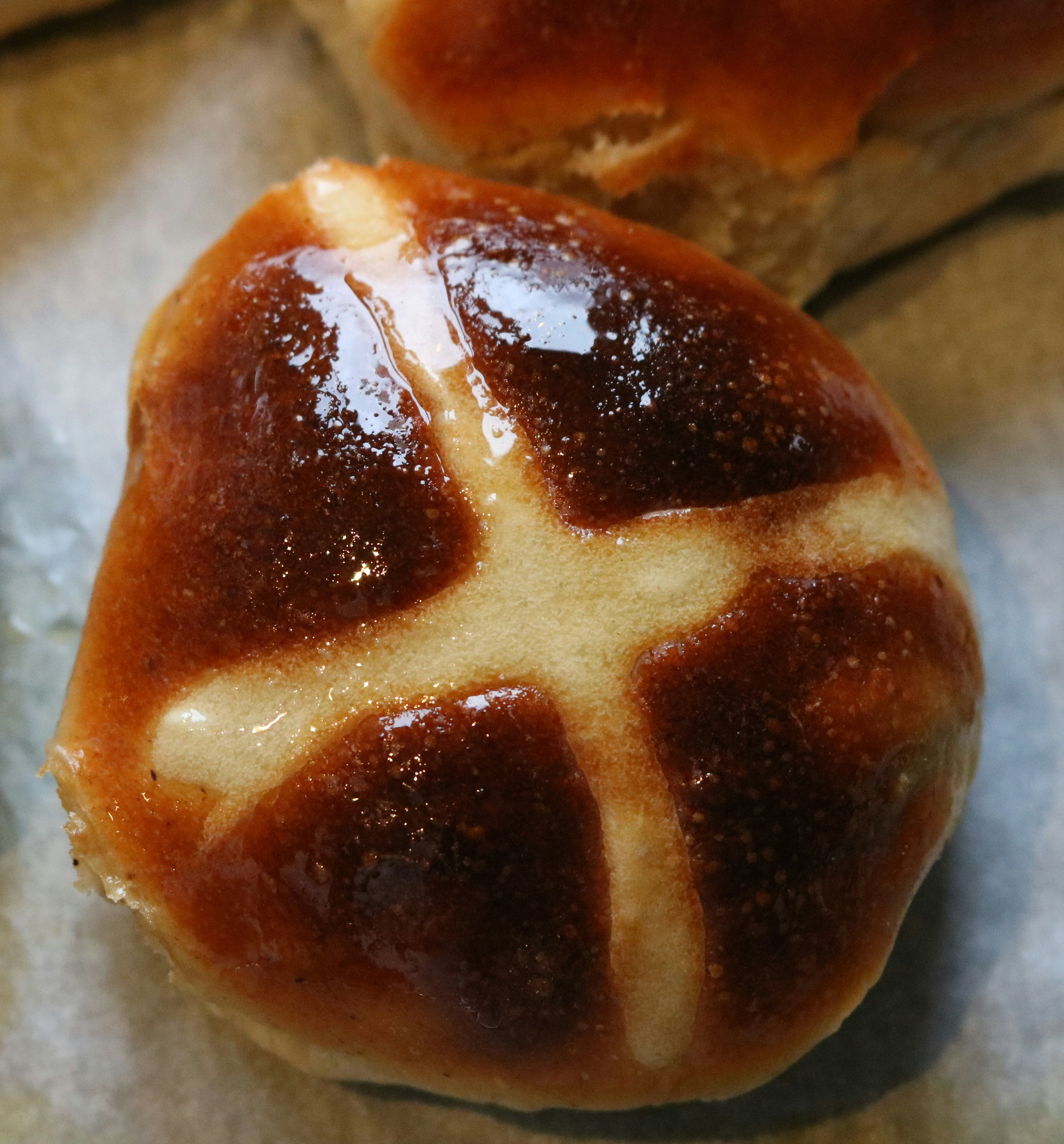 Close-up of a glazed hot cross bun on a baking tray