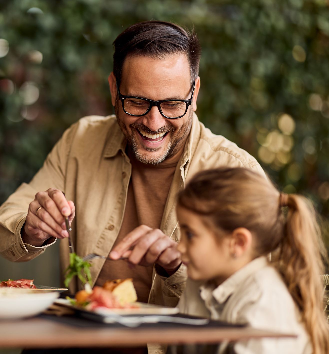 Smiling man enjoying a meal with a young girl at an outdoor restaurant