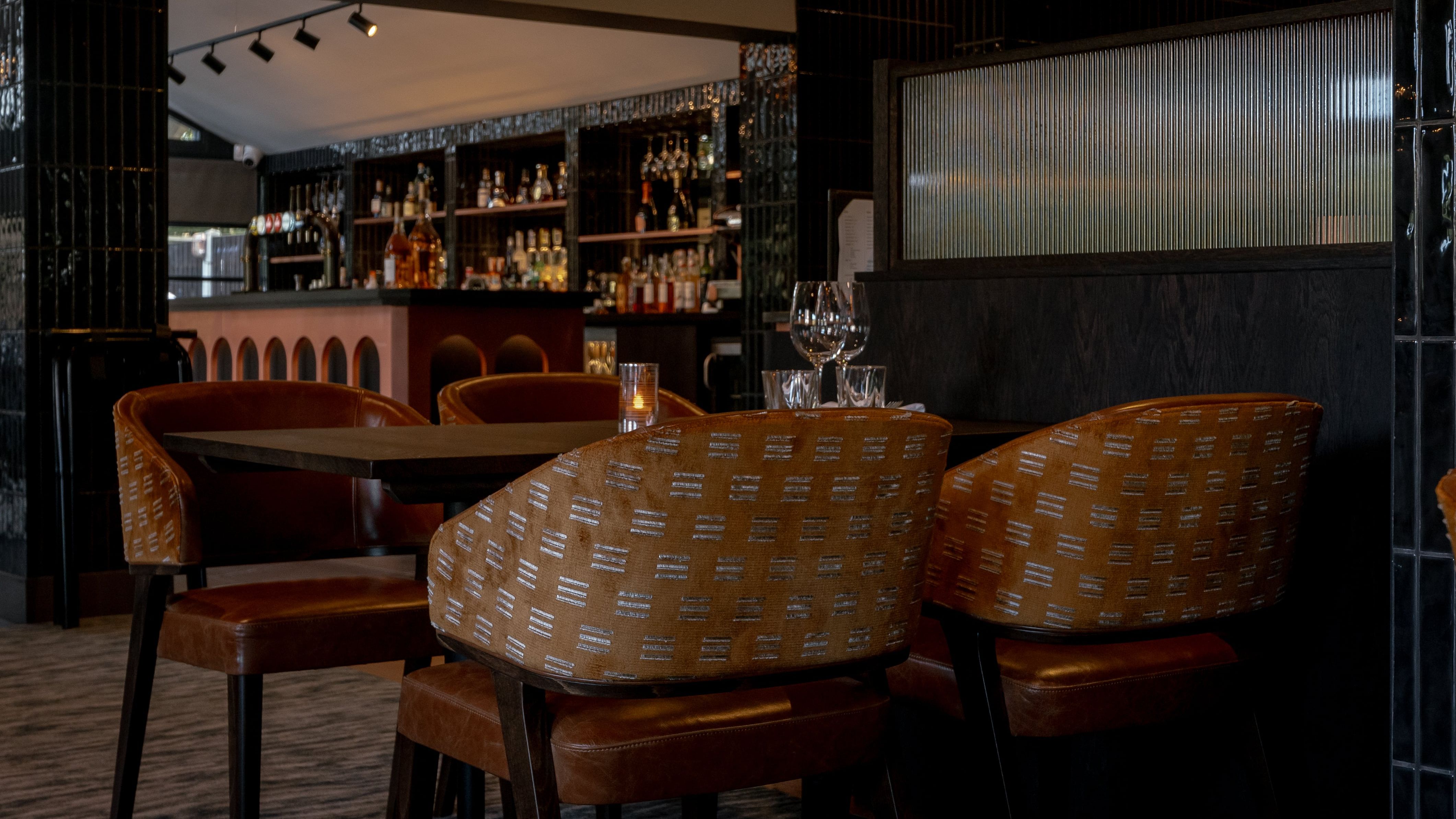 Modern restaurant dining area with brown chairs and a well-stocked bar in the background