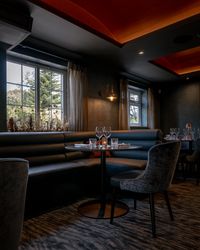 Elegant restaurant interior with a round table, cushioned booth seating, chairs, and set dining tableware near large windows.