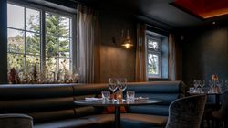 Elegant restaurant interior with a round table, cushioned booth seating, chairs, and set dining tableware near large windows.