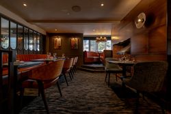 Elegant restaurant interior with orange and gray seating, tables set for dining, and warm lighting.